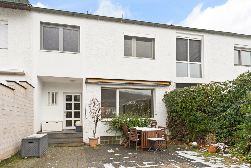 Rückseite eines Reihenhauses mit Terrasse, Gartenmöbeln und einigen Pflanzen.