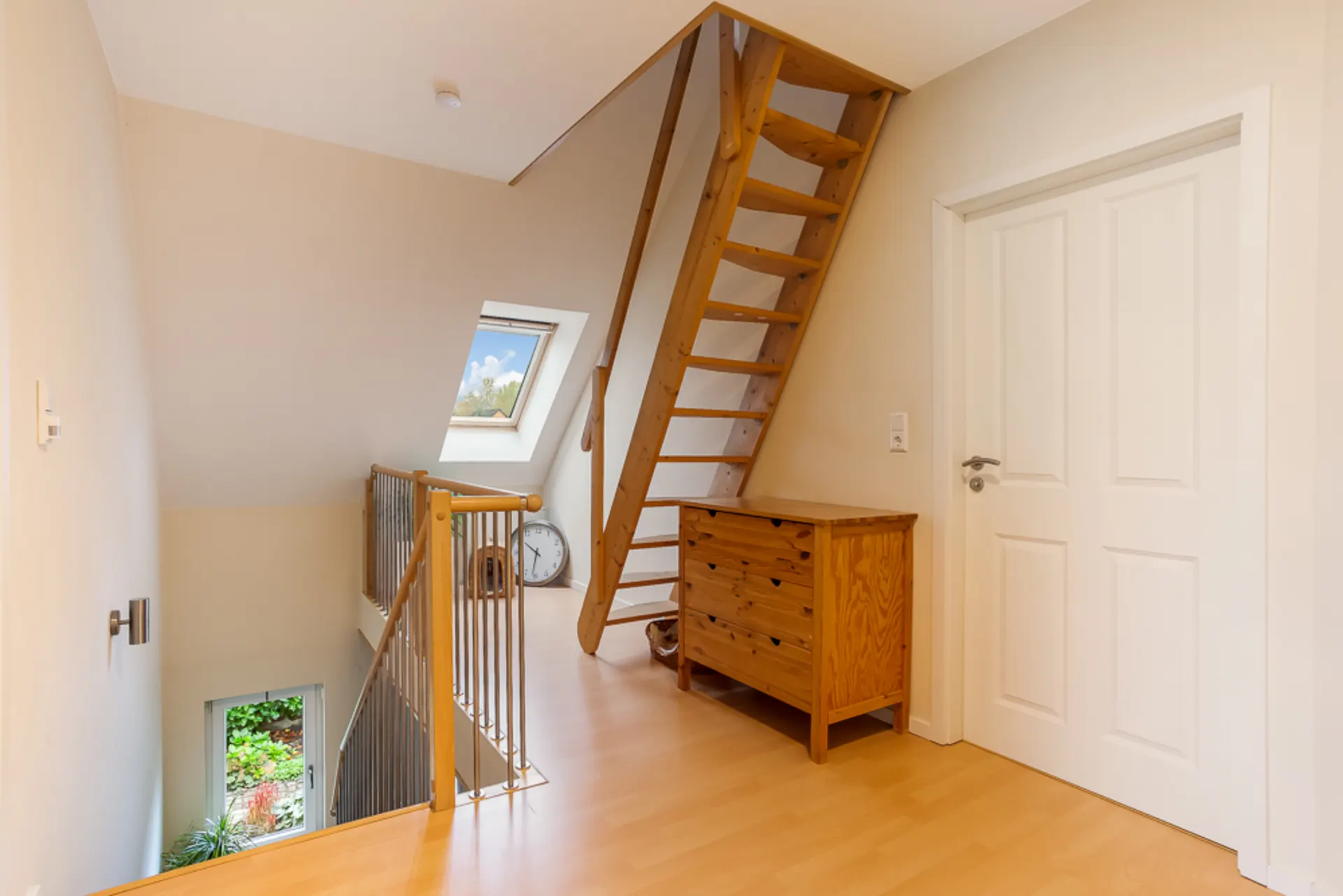 Heller Flur mit Holztreppe, Kommode, weißer Tür und Dachfenster.