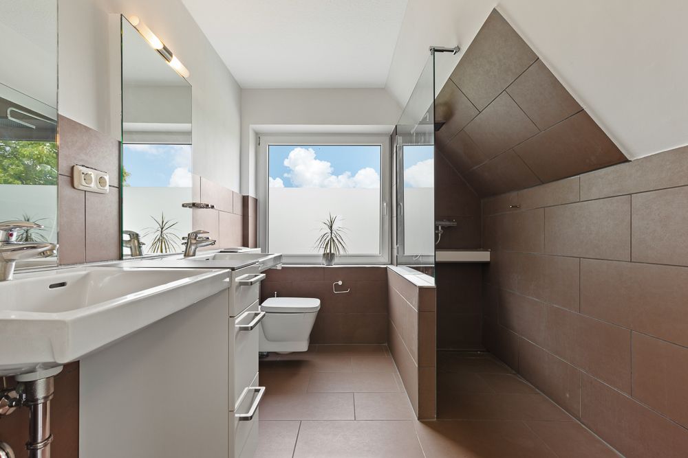 Modernes Badezimmer mit Doppelwaschbecken, Toilette, Dusche und großem Fenster.