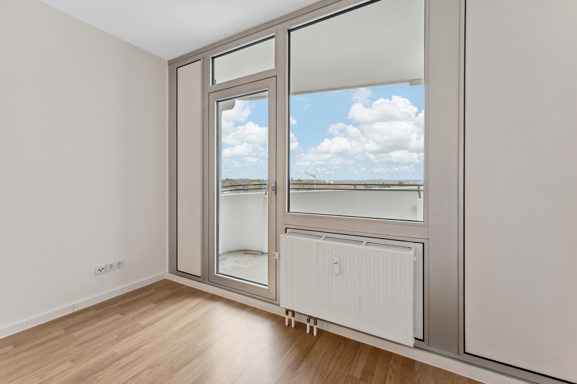 Helles Zimmer mit Holzfußboden, großer Fensterfront und Zugang zu einem Balkon.