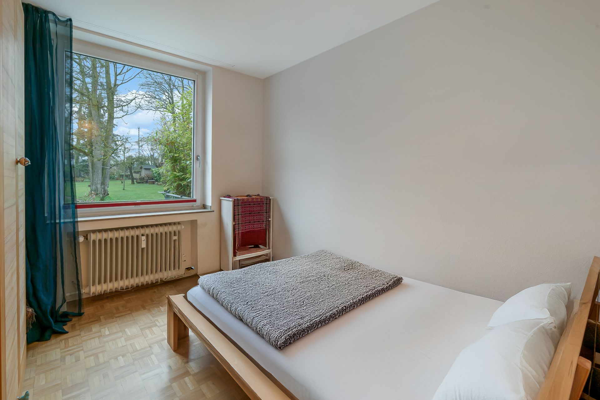 Kleines Schlafzimmer mit Holzbett, großem Fenster und Blick auf einen grünen Garten.