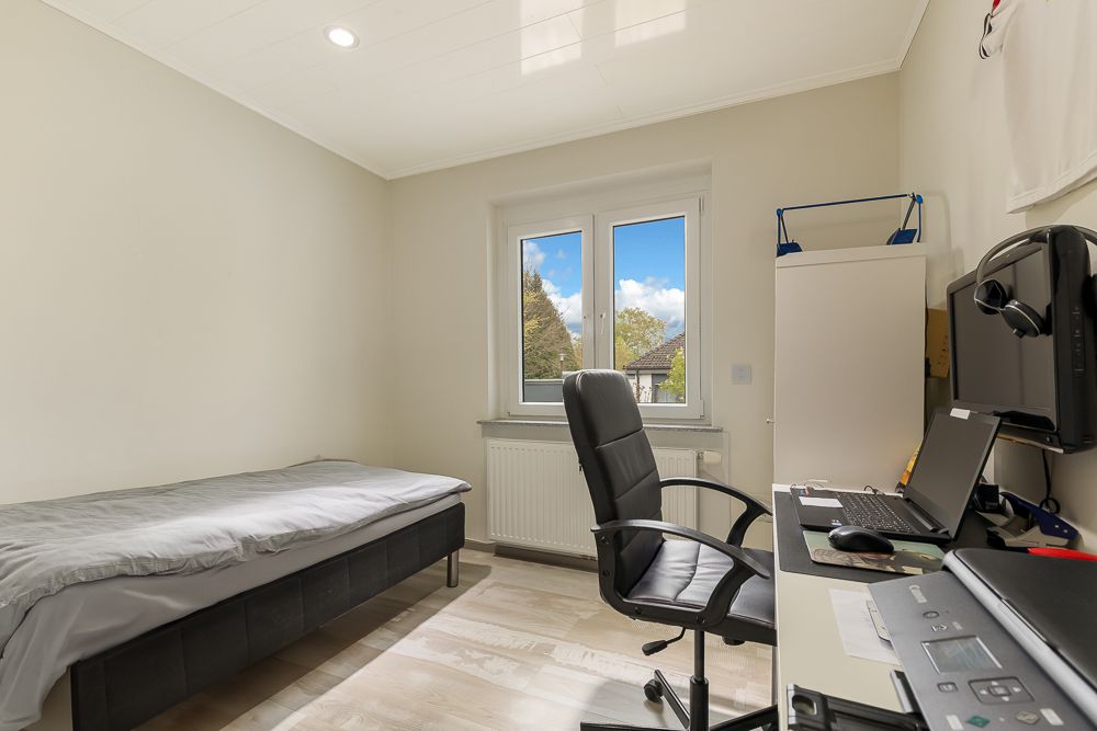 Helles Zimmer mit Bett, Schreibtisch, Bürostuhl und Fenster mit Blick ins Freie.