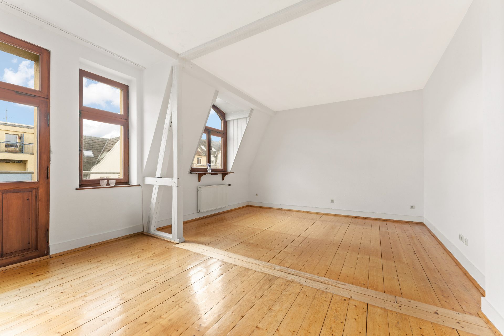 Helles Zimmer mit Holzboden, weißen Wänden und mehreren Fenstern.