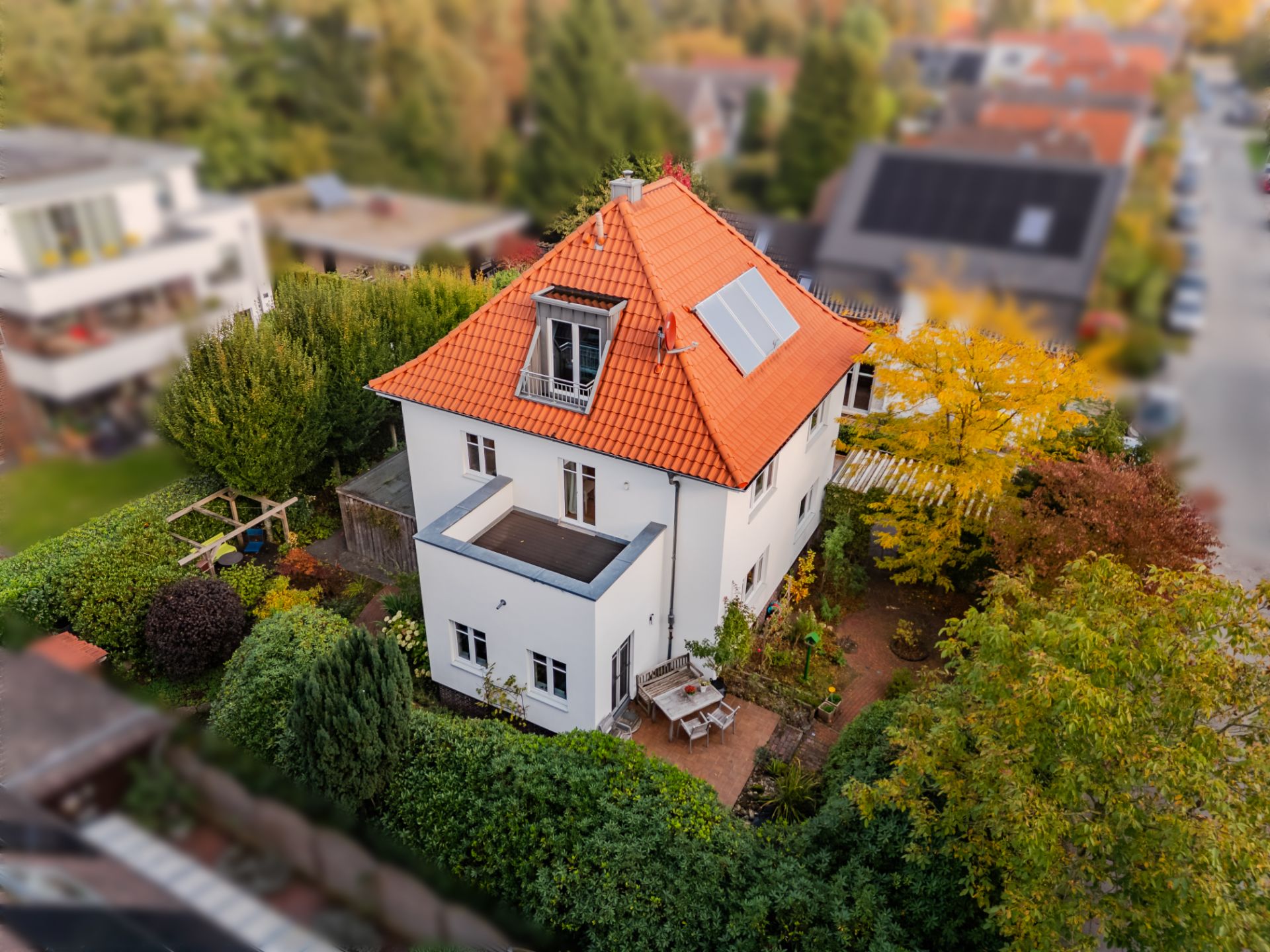 Weißes Wohnhaus mit rotem Dach, Solarpanel und Garten, von oben fotografiert.