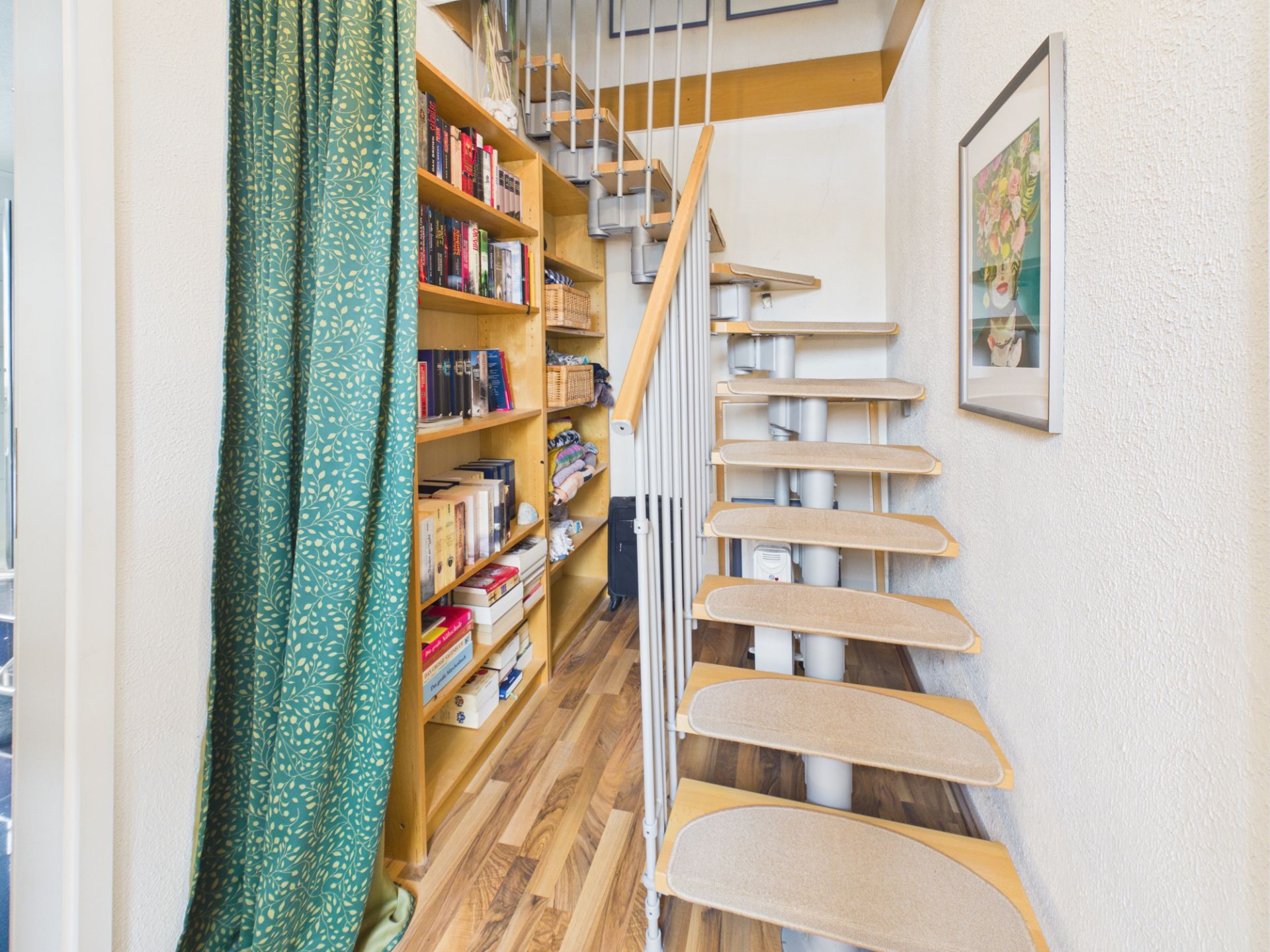 Moderne Holztreppe mit Bücherregal und grünem Vorhang in einem Wohnbereich.