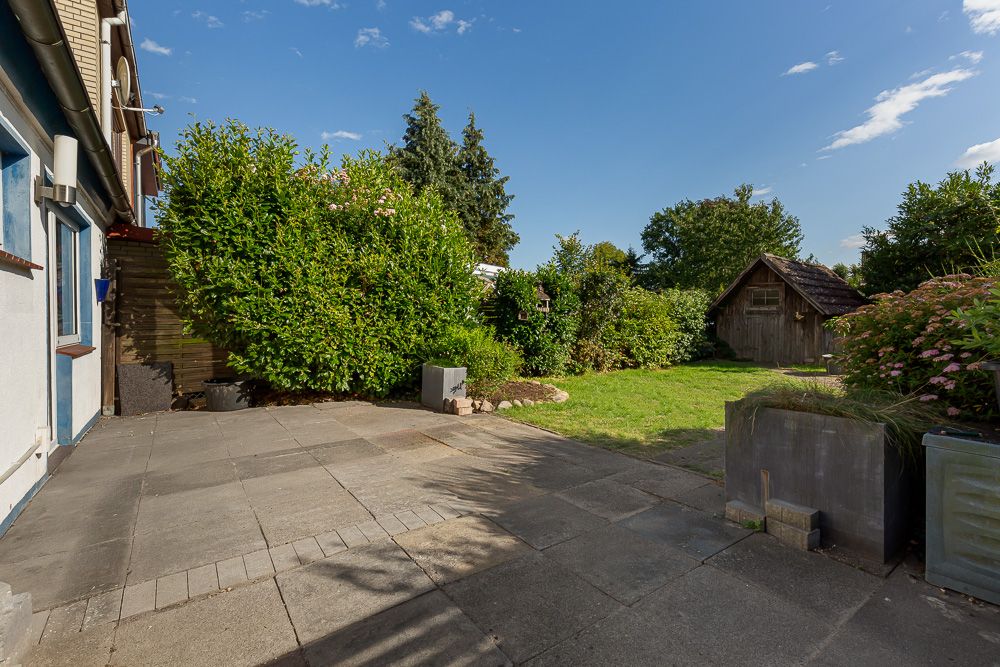 Gepflasterte Terrasse mit angrenzendem Garten und Holzschuppen im Hintergrund.