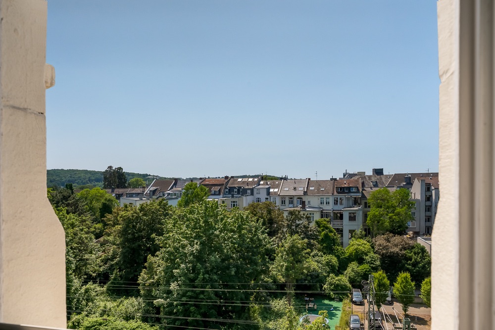 Blick aus einem Fenster auf Bäume und Wohnhäuser bei klarem Himmel.