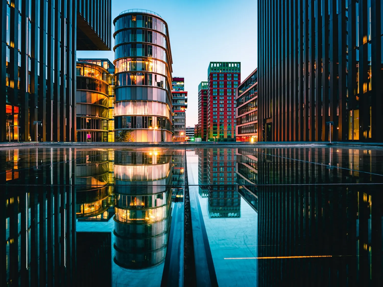 Moderne Wohngebäude mit Glasfassaden spiegeln sich in einer Wasserfläche.
