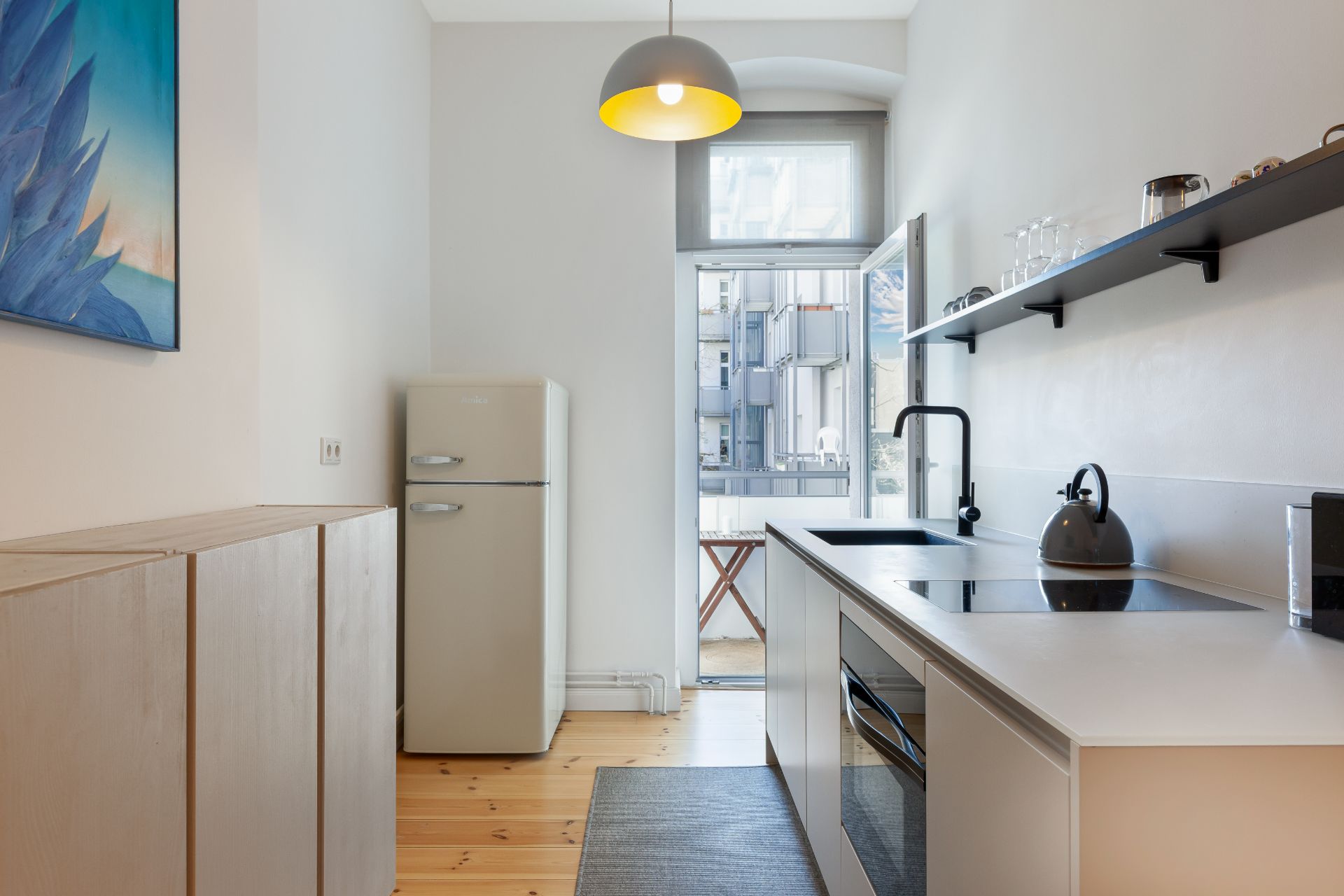 Moderne, schmale Küche mit Kühlschrank, Herd, Regal und Fenster zur Terrasse.