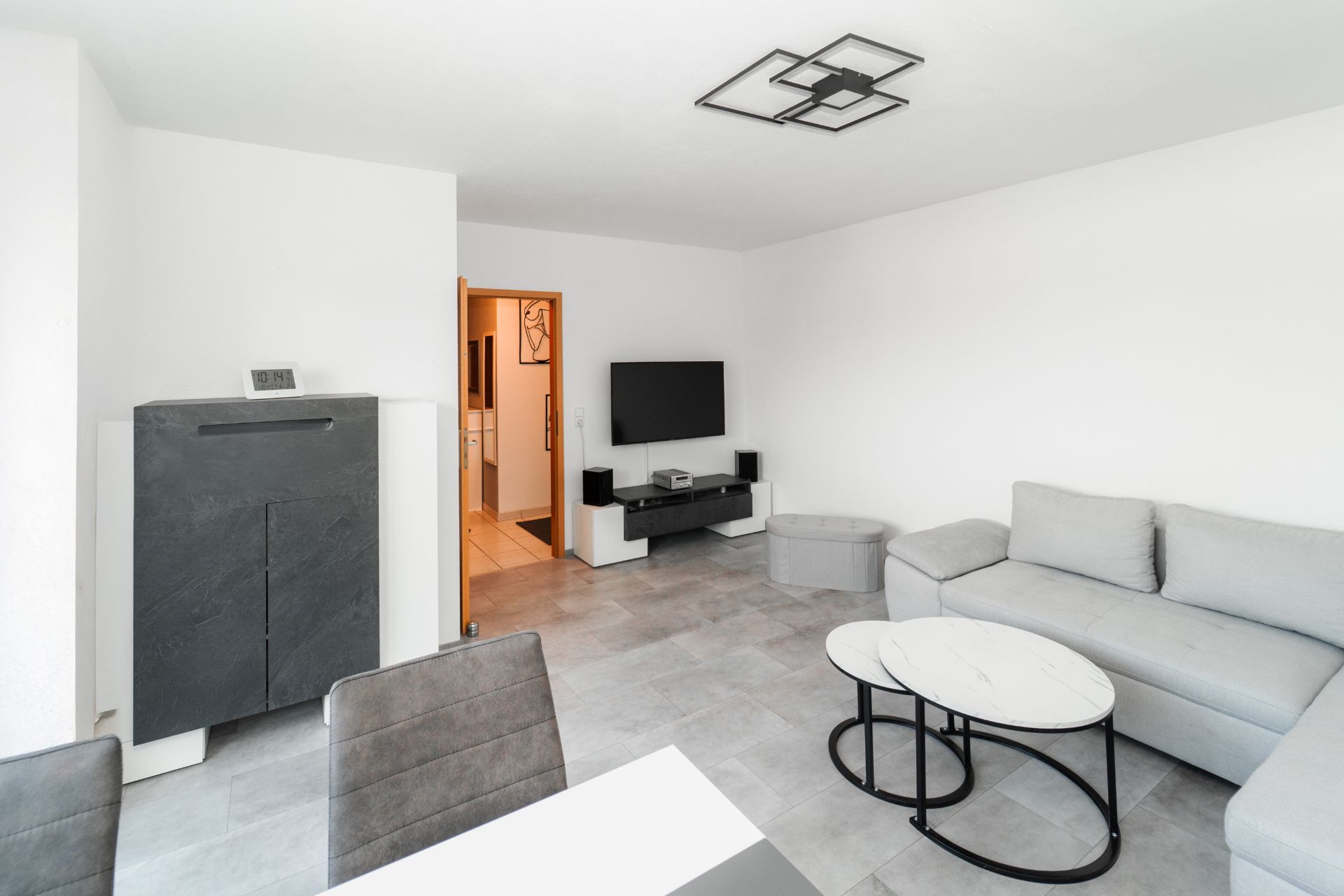 Modernes Wohnzimmer mit grauem Sofa, Couchtisch, Fernseher und Esstisch mit Stühlen.