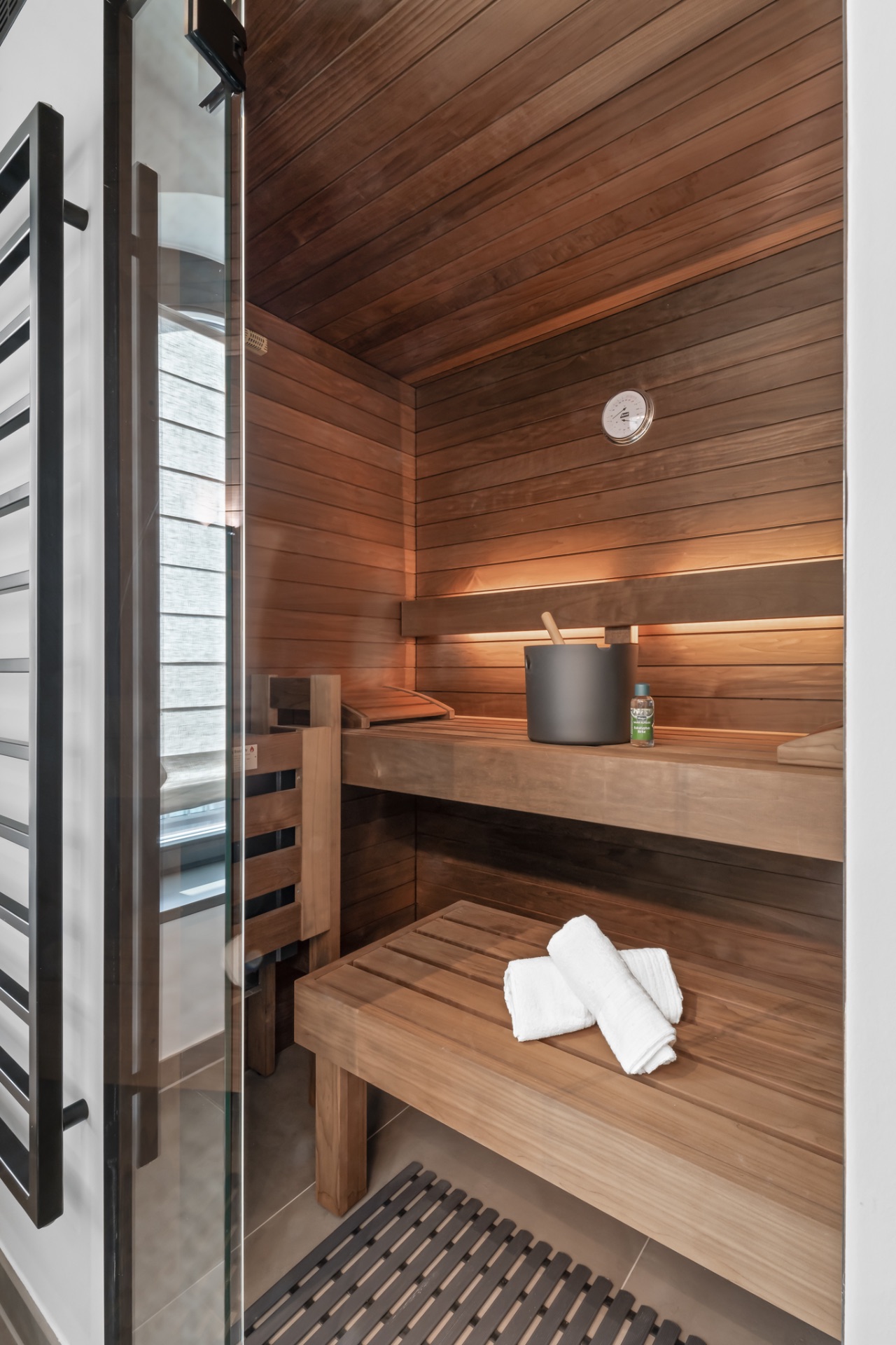 Moderne Holzsauna mit Handtüchern und Saunaeimer auf der Bank.