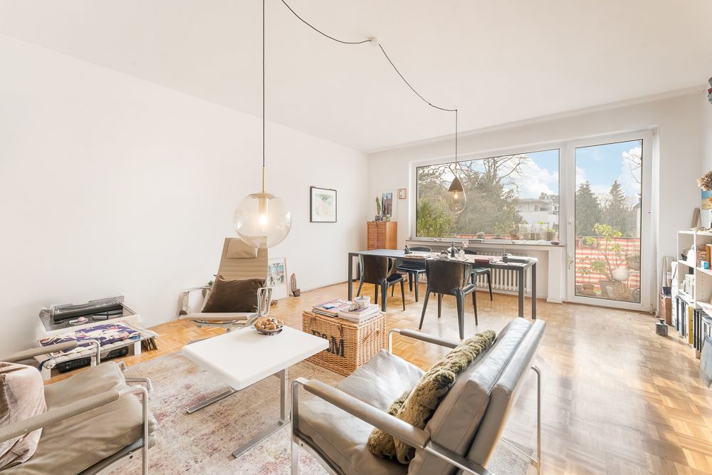 Helles Wohnzimmer mit großen Fenstern, Sitzgruppe, Esstisch und Regal, Blick auf Balkon und Garten.