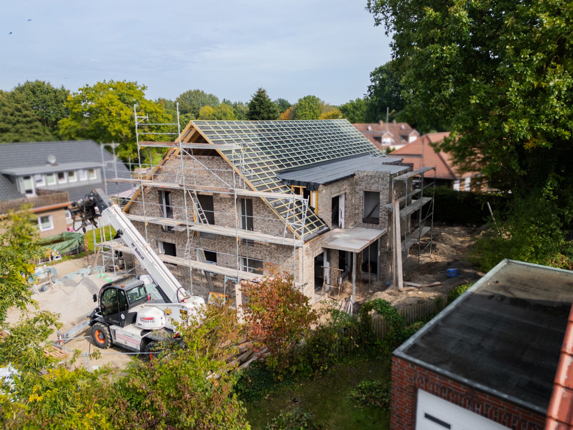Ein zweistöckiges Wohnhaus im Rohbau mit Baugerüst und Kran auf der Baustelle.