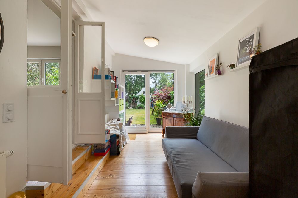 Helles Wohnzimmer mit grauem Sofa, Holzboden und Zugang zum Garten durch Glastüren.