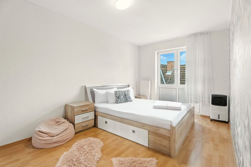 Helles Schlafzimmer mit Doppelbett, Nachttisch, Sitzsack, Fenster und Holzfußboden.