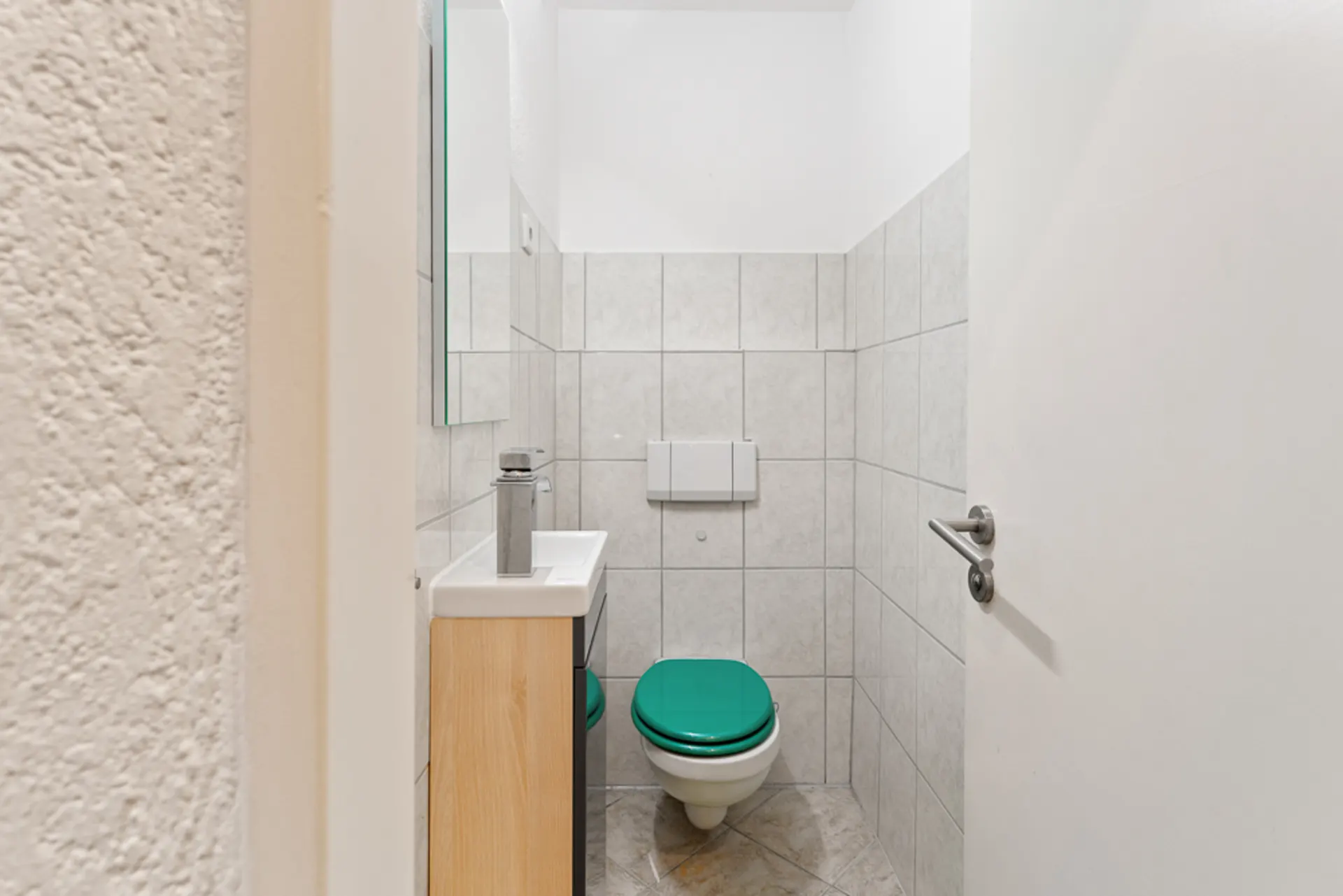 Kleines Badezimmer mit Toilette, grünem Toilettensitz und kleinem Waschbecken.