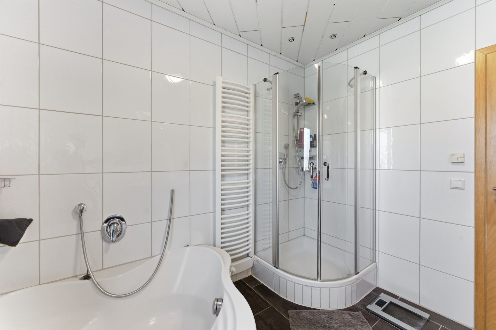 Helles Bad mit Eckdusche, Badewanne und Handtuchheizkörper, weiße Fliesenwände.