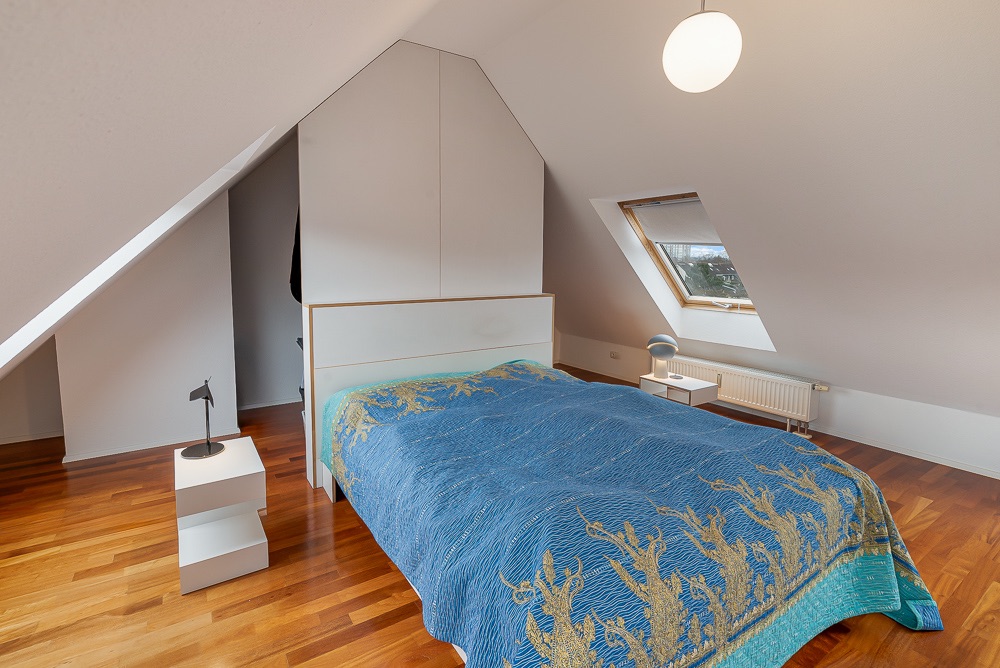 Schlafzimmer mit Dachschräge, großem Bett, Holzfußboden und Dachfenster.