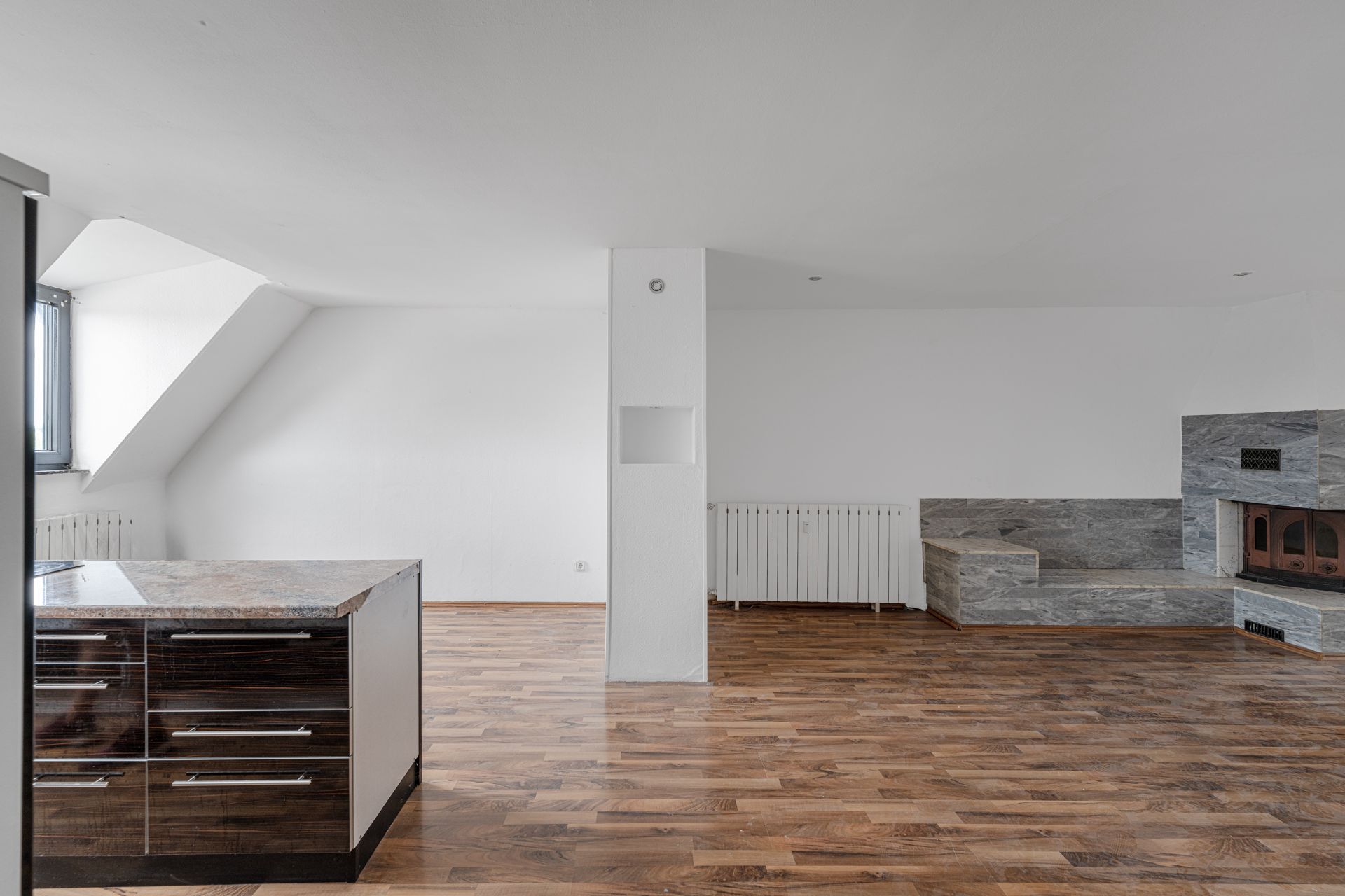 Heller Raum mit Holzfußboden, Kücheninsel und gemauertem Kamin in der Ecke.