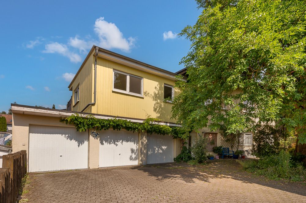 Doppelgarage mit gelbem Wohnhaus darüber, Hof und Baum rechts im Bild.