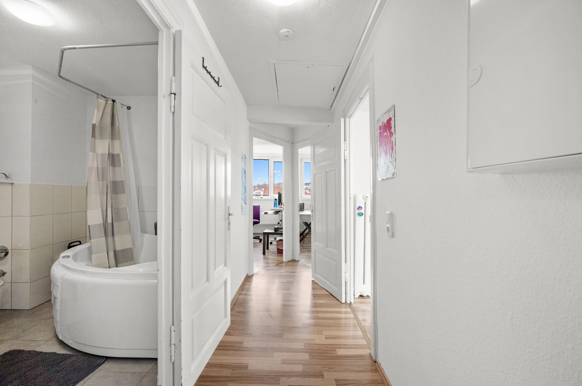 Heller Flur mit Blick ins Badezimmer und ein Zimmer mit großem Fenster im Hintergrund.