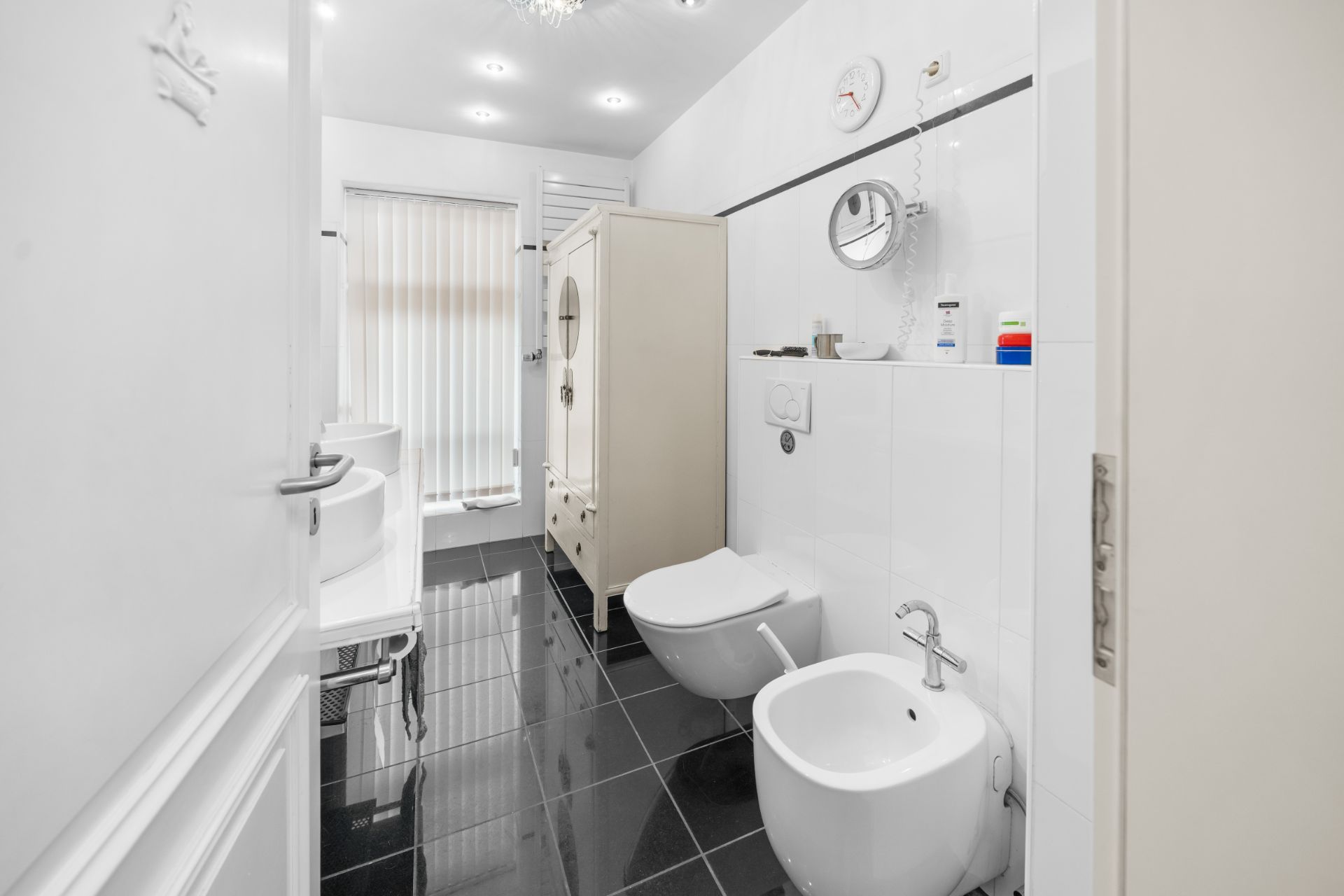 Modernes Badezimmer mit schwarzen Fliesen, Bidet, WC, Waschtisch und Schrank.