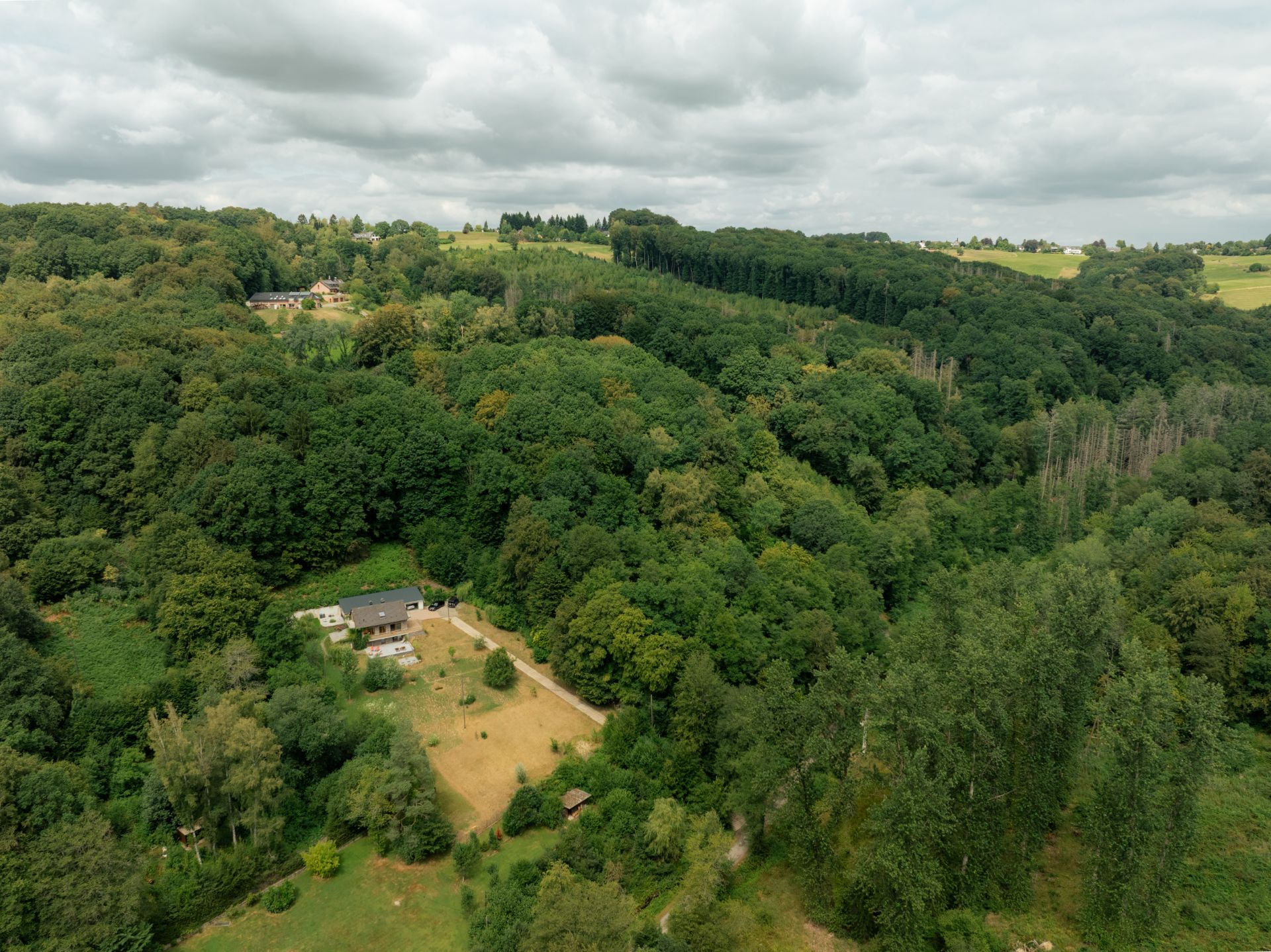 Luftaufnahme eines Hauses am Waldrand mit großem Garten, umgeben von dichtem Wald.