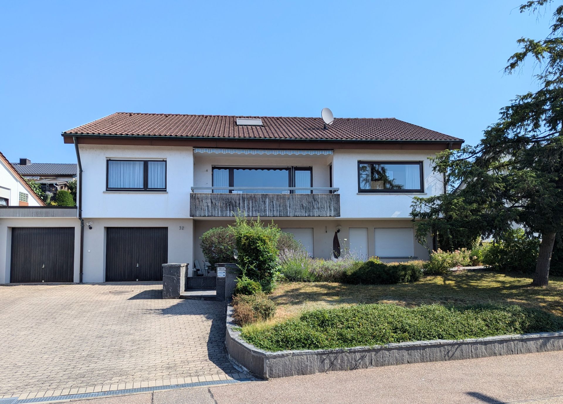 Zweistöckiges Wohnhaus mit rotem Dach, Balkon, zwei Garagen und gepflegtem Vorgarten.