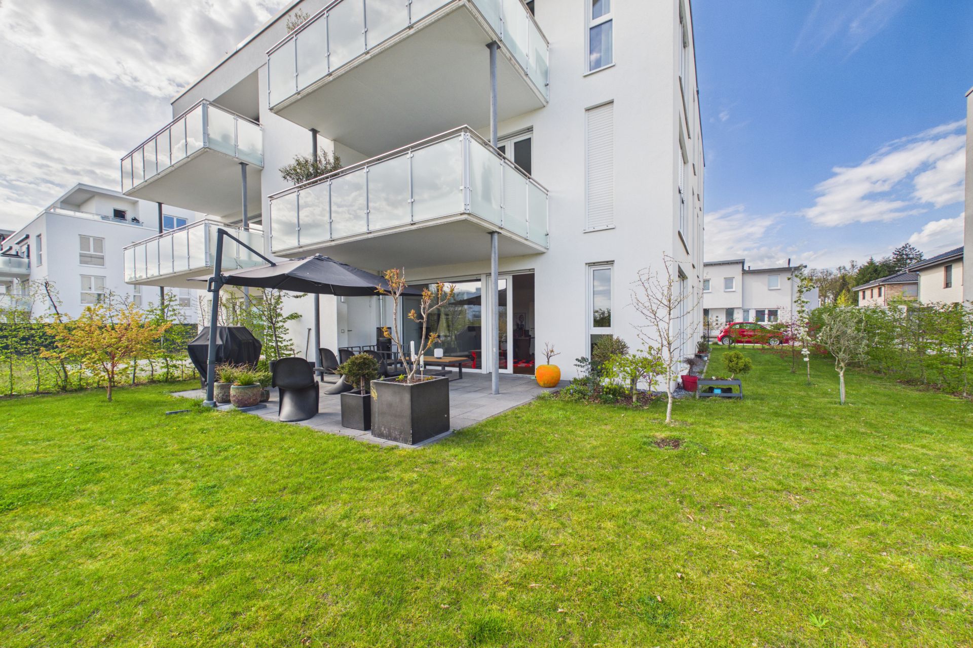 Moderne Wohnung mit Balkon und Terrasse, umgeben von grünem Rasen und Pflanzen.