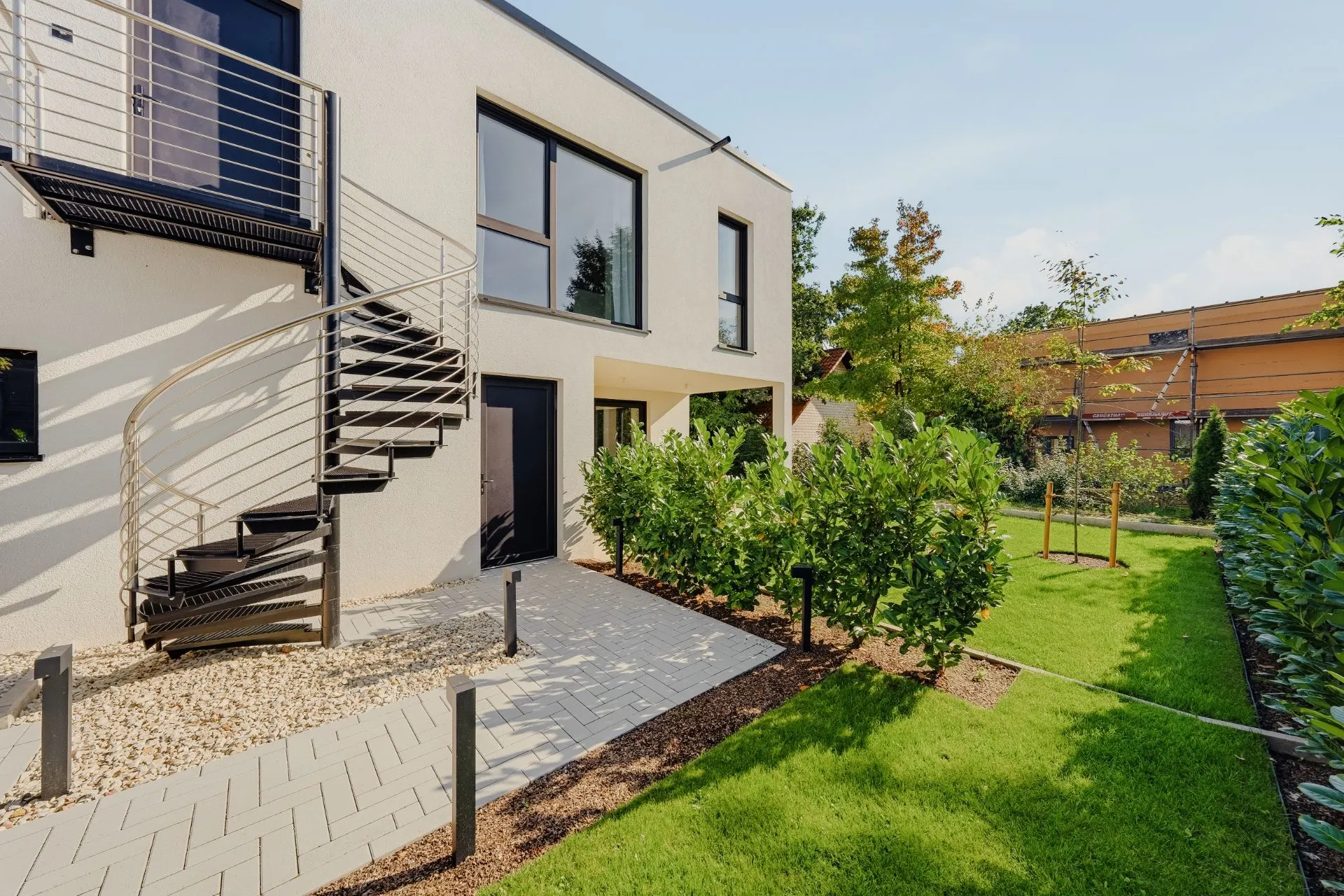 Moderner Wohnhausgarten mit Wendeltreppe, großen Fenstern und gepflegtem Rasen.
