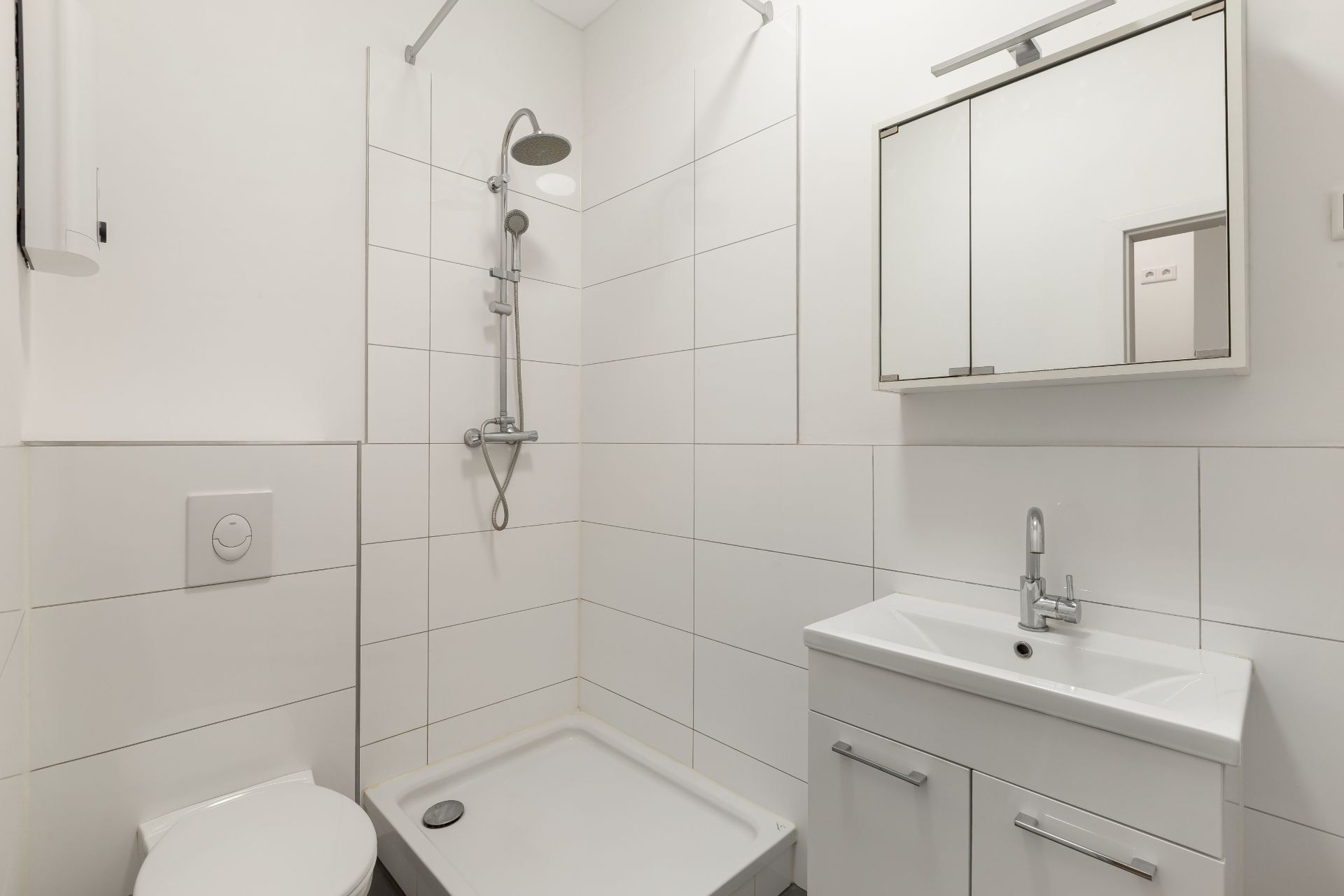 Modernes, weiß gefliestes Badezimmer mit Dusche, Waschbecken, Spiegel und Toilette.