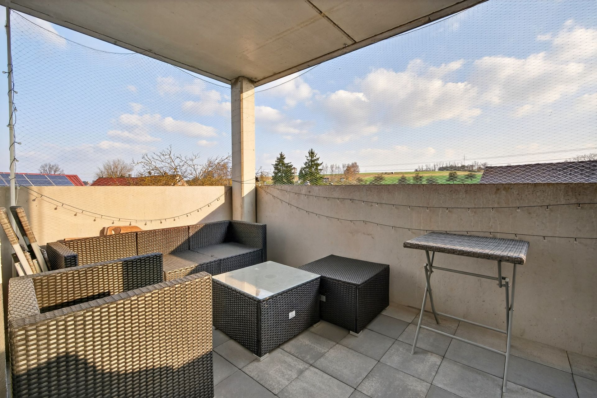 Überdachte Terrasse mit Korbmöbeln und Blick ins Grüne.