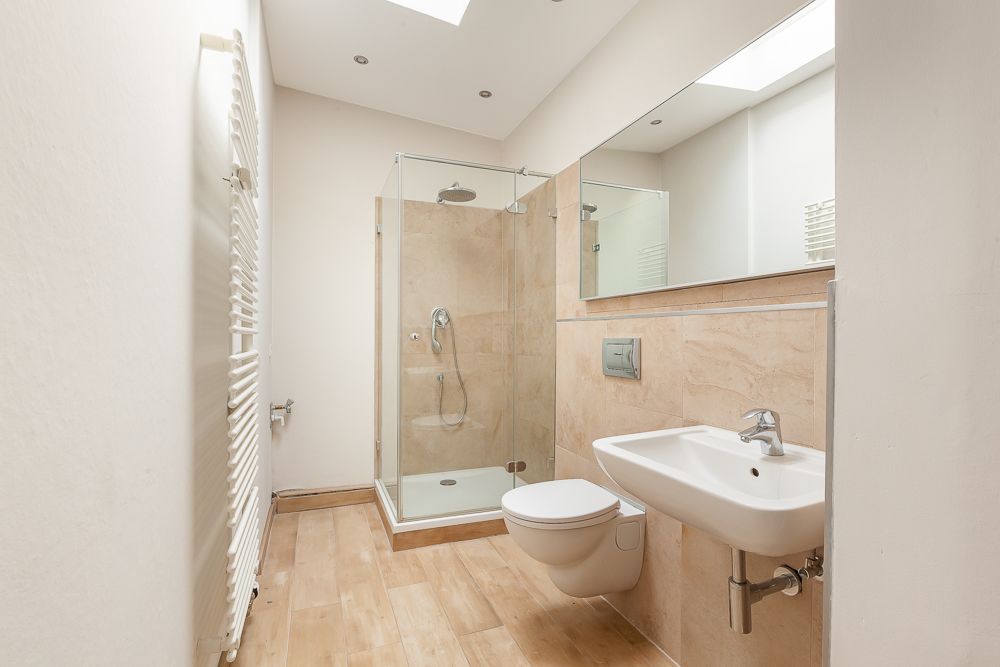 Modernes Badezimmer mit Dusche, Wandtoilette und Waschbecken, helle Fliesen und großem Spiegel.