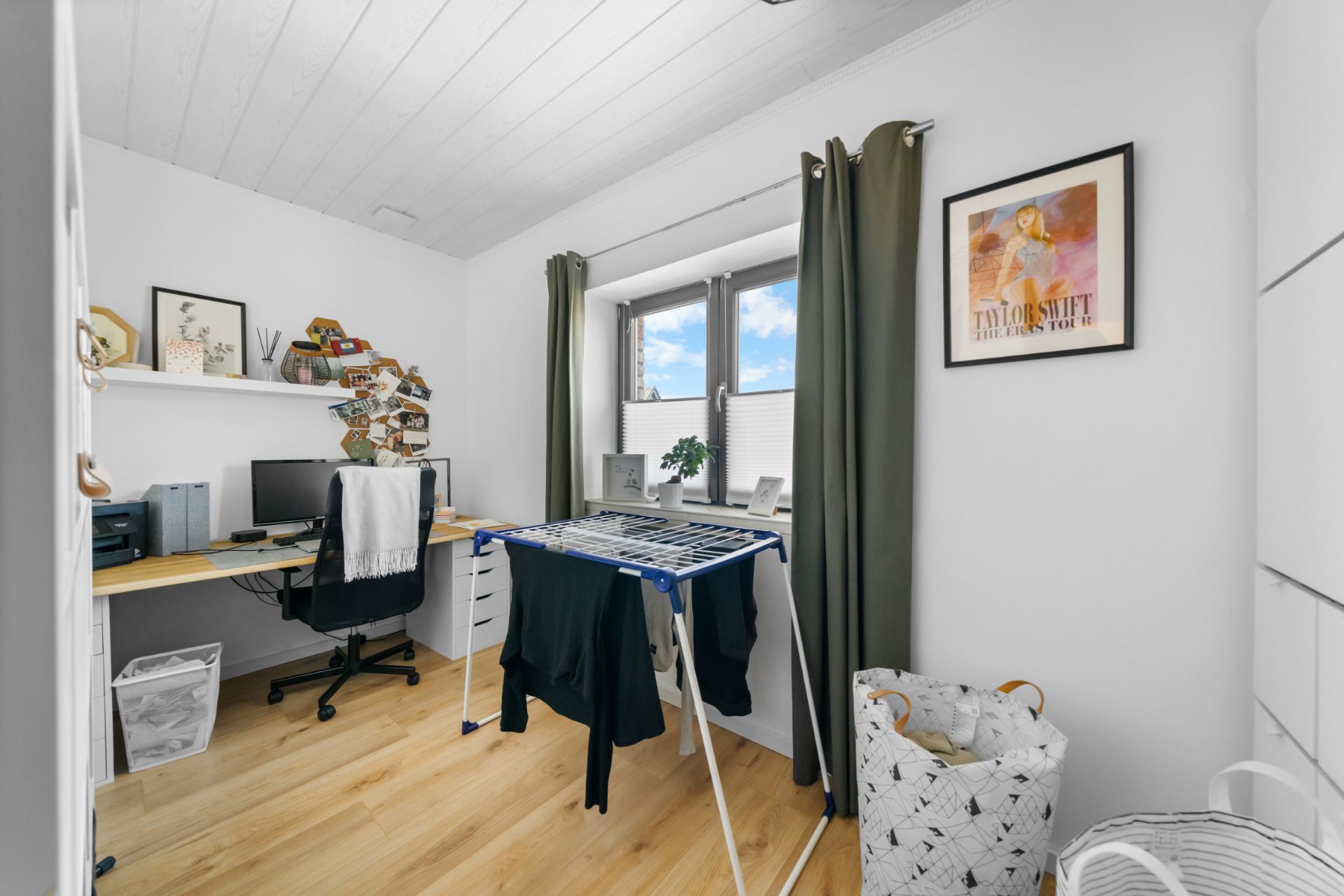 Helles Arbeitszimmer mit Schreibtisch, Wäscheständer, Fenster und Wanddekoration.