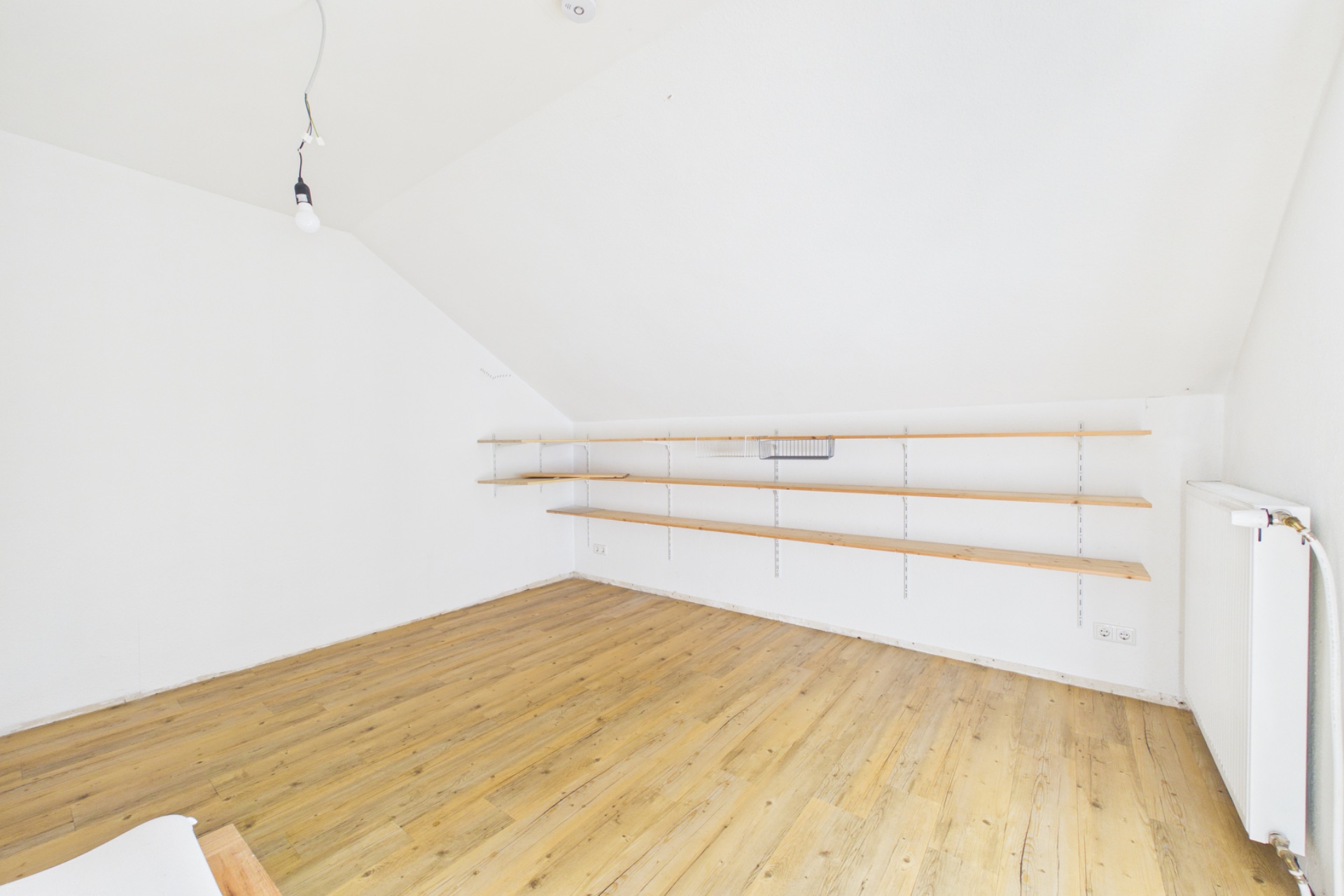 Heller leerer Raum mit Holzfußboden, weißen Wänden und drei Wandregalen.