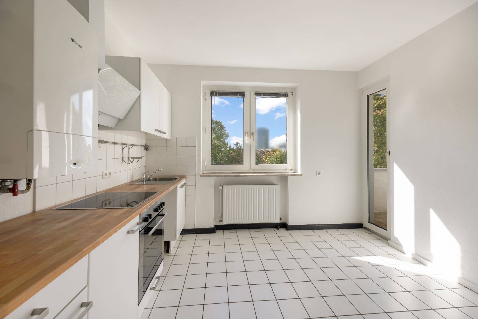 Helle Küche mit weißen Fliesen, Holzarbeitsplatte und Fenster mit Blick ins Grüne.