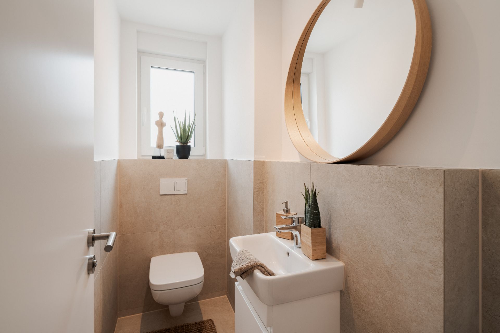 Modernes kleines Bad mit WC, Waschbecken, rundem Spiegel und Fenster.