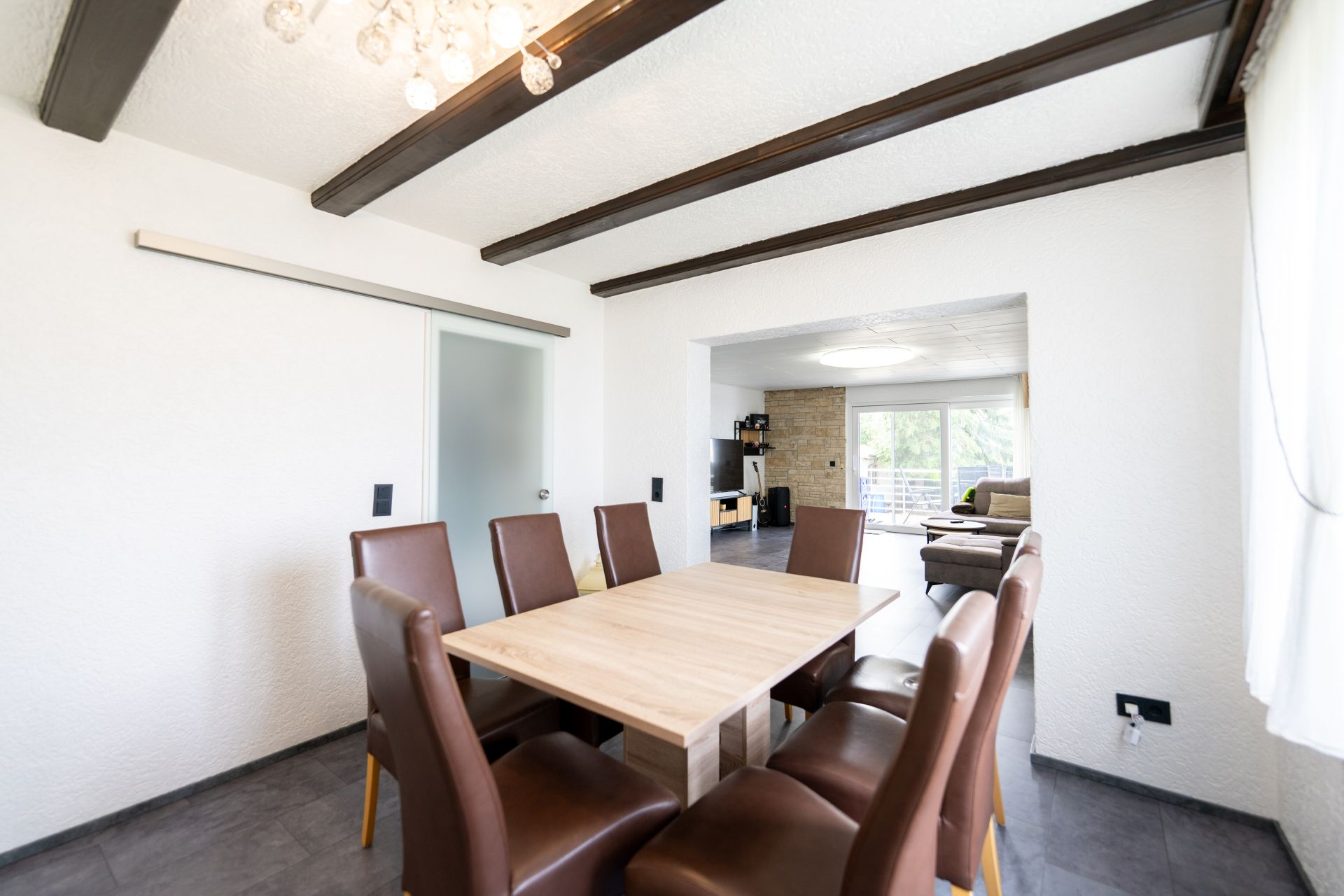 Esszimmer mit Holztisch und sechs braunen Stühlen, angrenzend an ein Wohnzimmer mit Sofa.