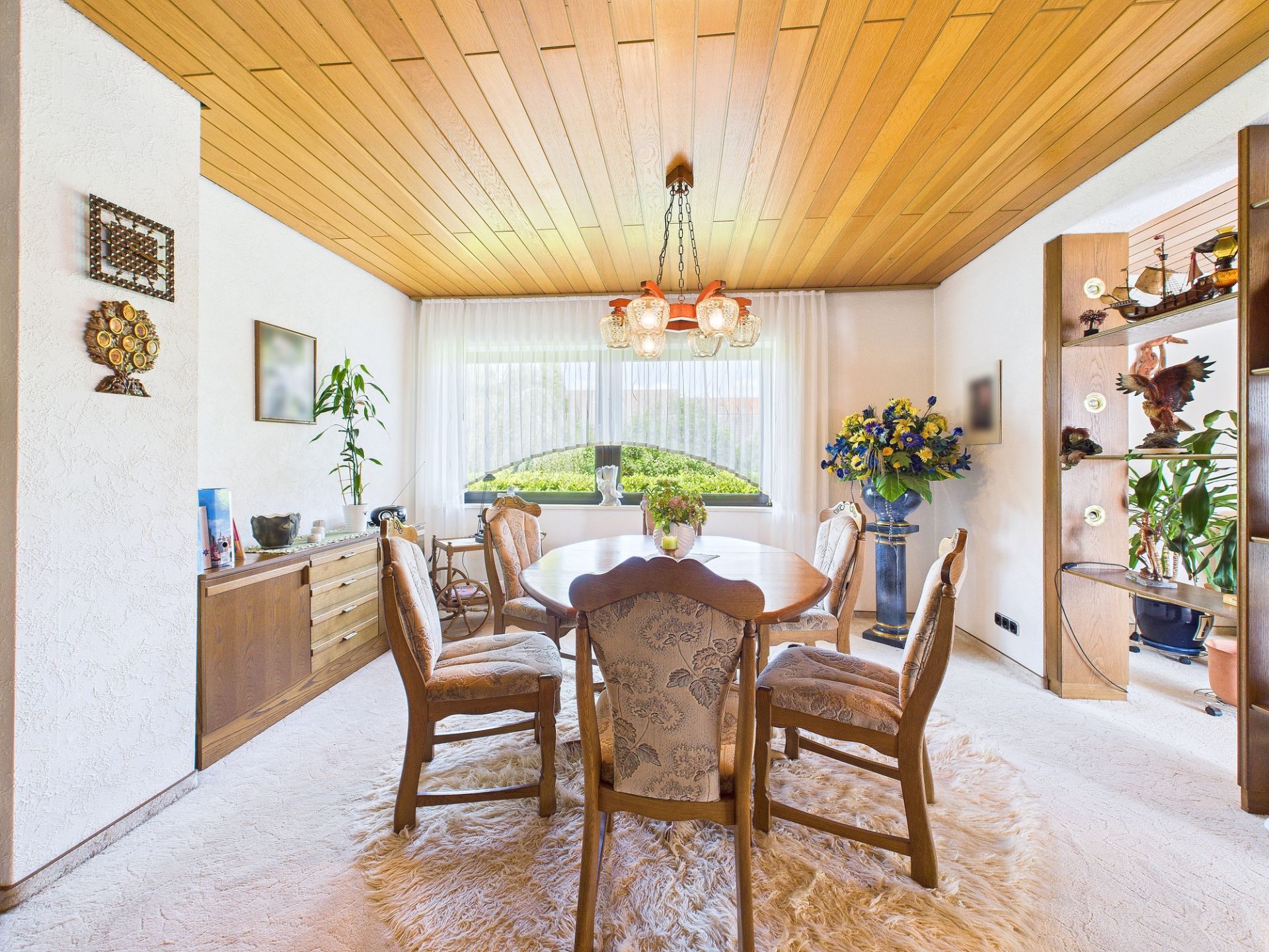 Esszimmer mit Holztisch, sechs Stühlen, Teppich und großem Fenster mit Vorhängen.