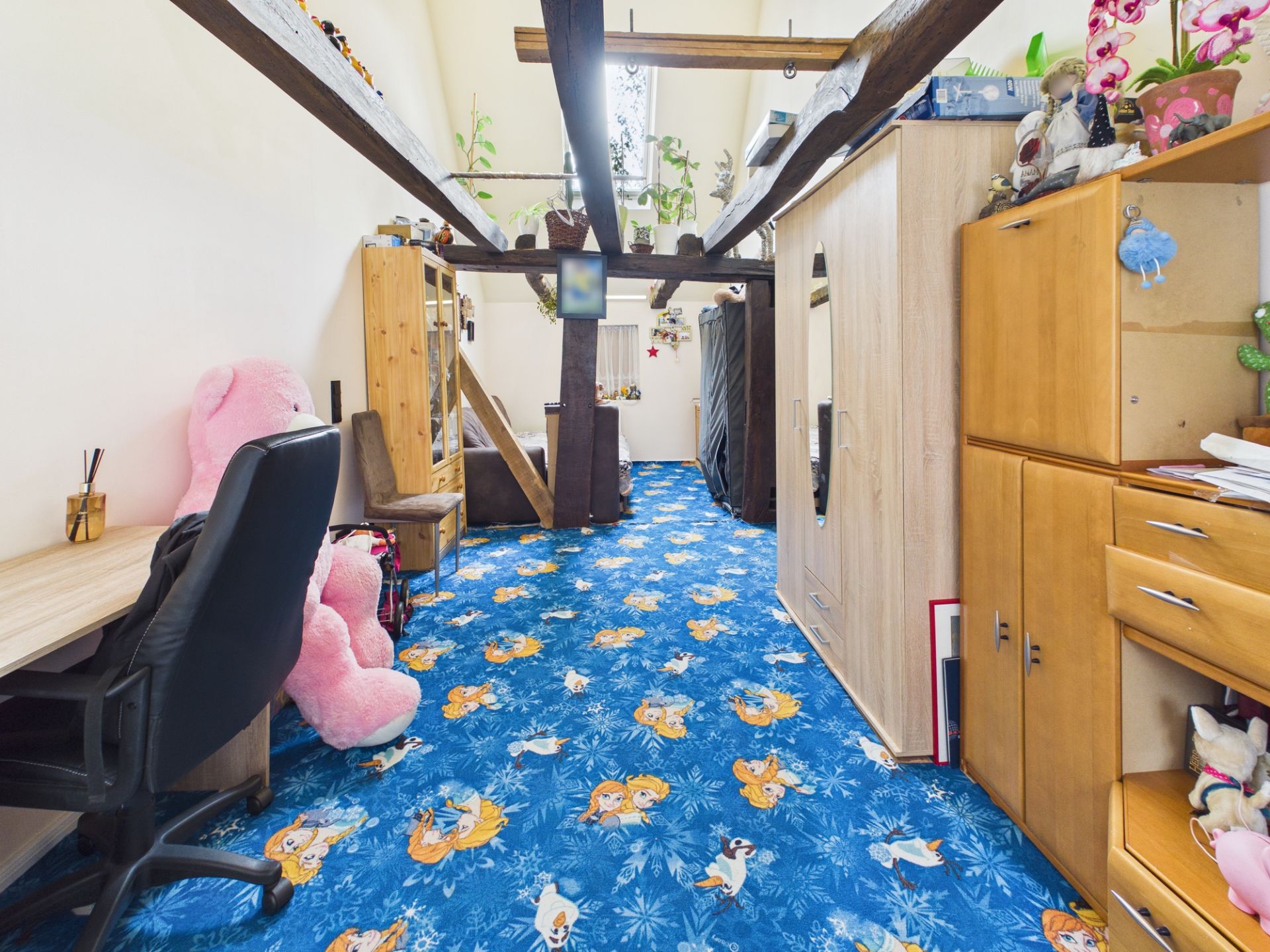 Kinderzimmer mit blauem Teppich mit Tiermotiven, Holzbalken und Spielzeug auf dem Schreibtisch.