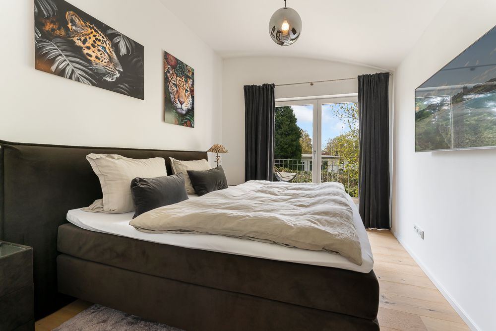 Modernes Schlafzimmer mit großem Bett, zwei Tigerbildern und Fenster mit Blick ins Grüne.