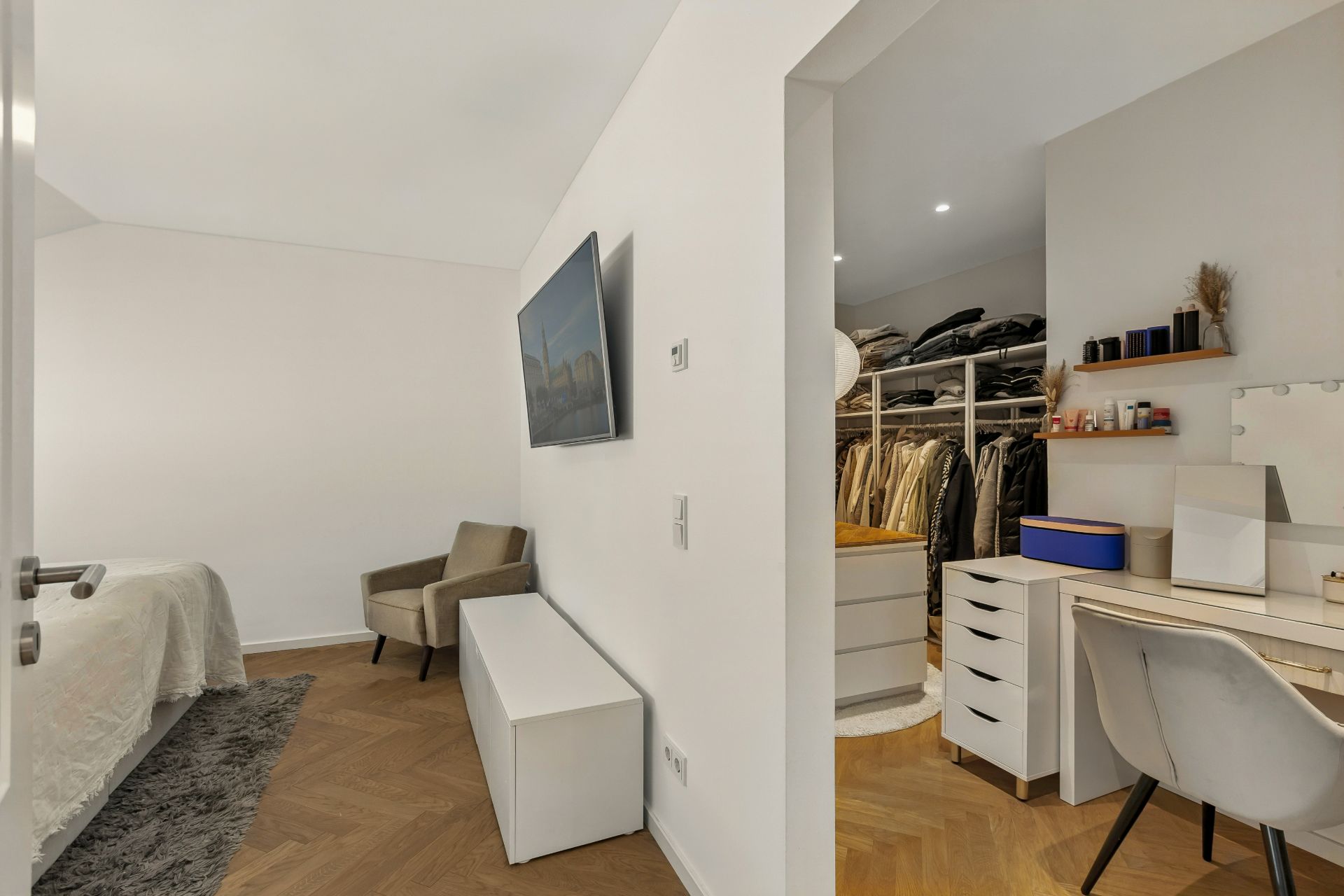 Modernes Schlafzimmer mit Fernseher, Sessel und begehbarem Kleiderschrank mit Schminktisch.