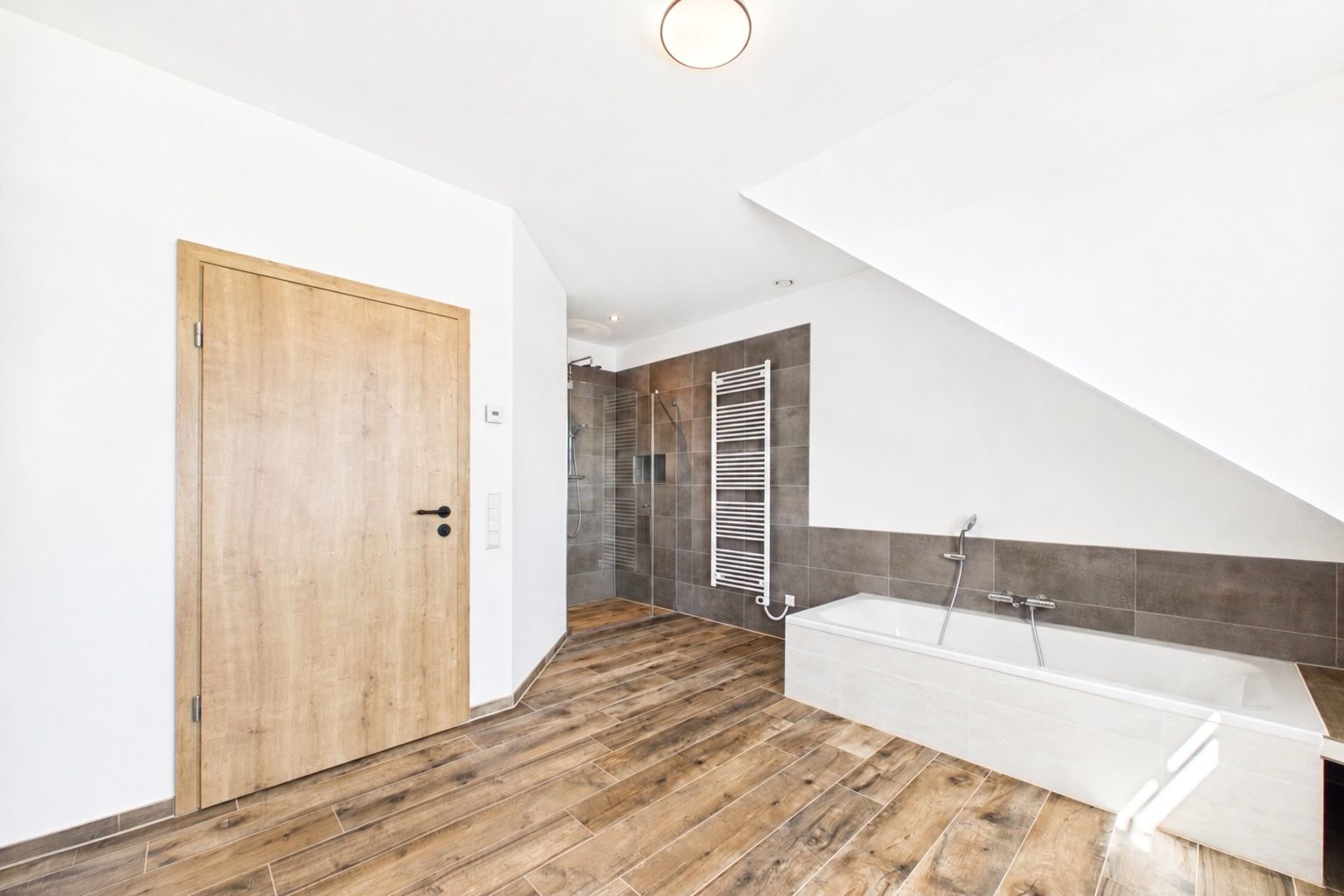 Modernes Bad mit Holzboden, Badewanne, Dusche, Handtuchheizkörper und Holztür.