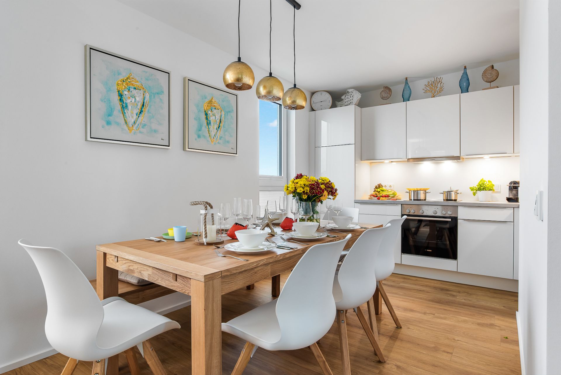 Moderne Küche mit Essbereich, Holztisch, weißen Stühlen und gelben Hängelampen.
