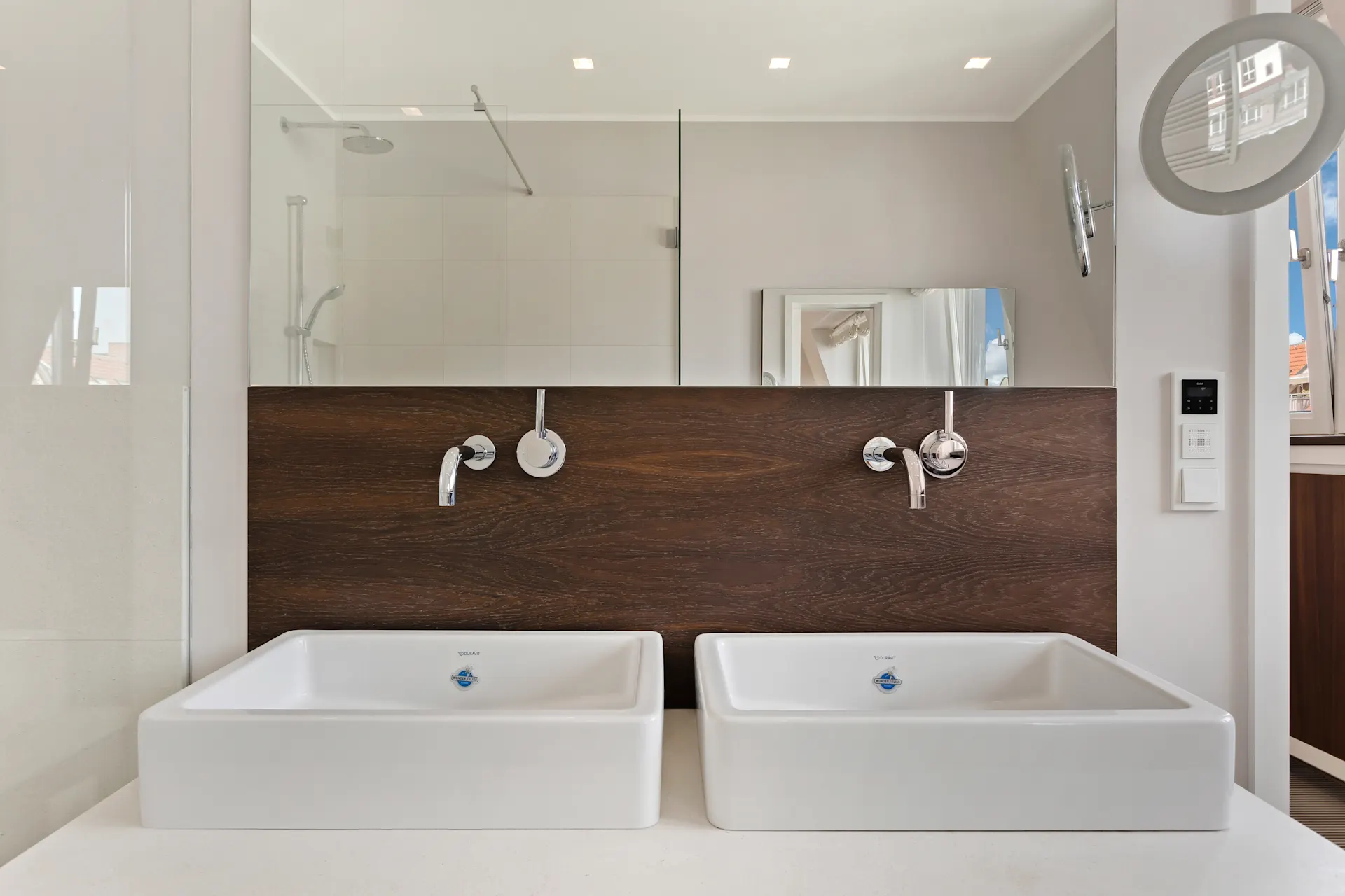 Zwei moderne weiße Waschbecken mit Wandarmaturen vor Holzverkleidung im Badezimmer.