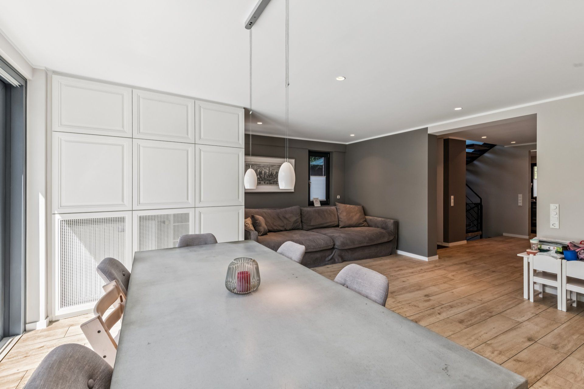 Modernes Wohnzimmer mit grauem Sofa, Esstisch, Holzfußboden und Hängelampen.