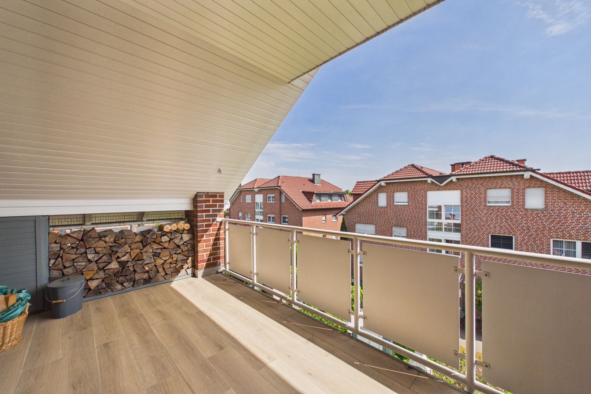 Überdachter Balkon mit Holzstapel und Blick auf benachbarte Wohnhäuser.