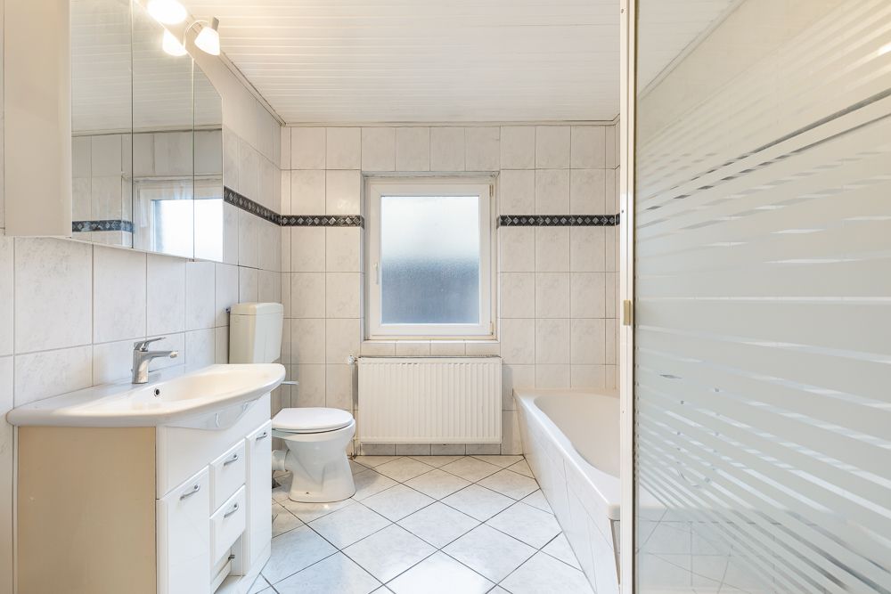 Helles Badezimmer mit Waschbecken, Toilette, Badewanne und Fenster.