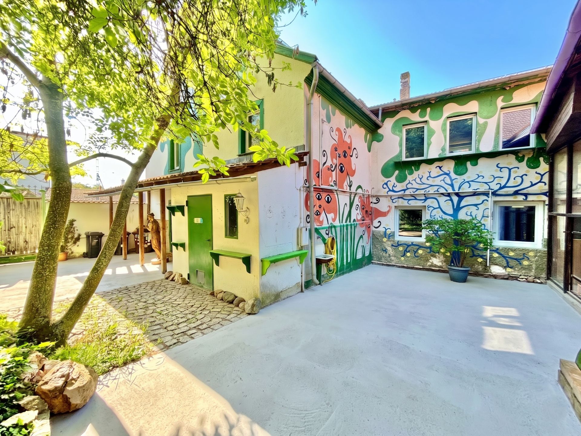 Bunter Innenhof mit bemalten Hauswänden, Bäumen und Pflastersteinen.