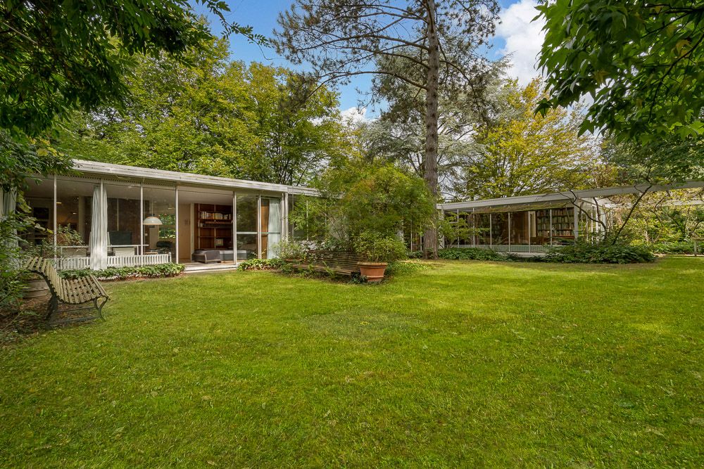 Zwei moderne Flachbauten mit großen Glasfronten in einem grünen Garten.